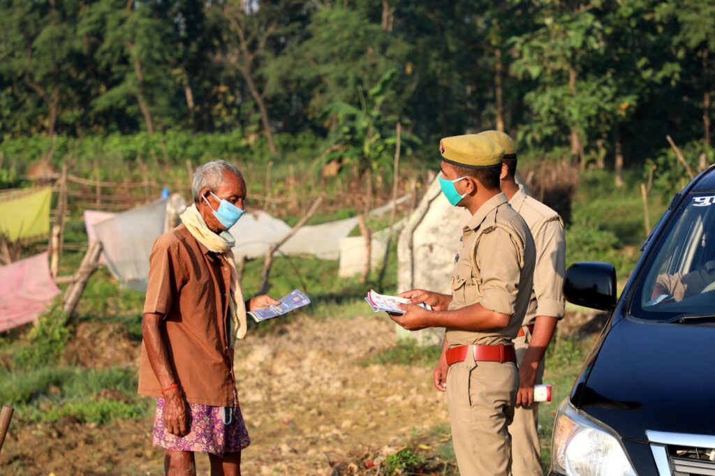 Police officers distribute flyers to a masked villager outdoors, emphasizing safety during the pandemic.