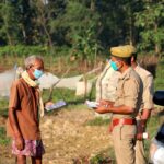 Police officers distribute flyers to a masked villager outdoors, emphasizing safety during the pandemic.