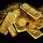 A close-up of gold bars and coins symbolizing wealth and investment on a black background.