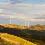 Wind turbines on green hills showcase renewable energy amidst a scenic landscape under a cloudy sky.