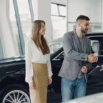Customers shaking hands with dealer in showroom, sealing car purchase deal.
