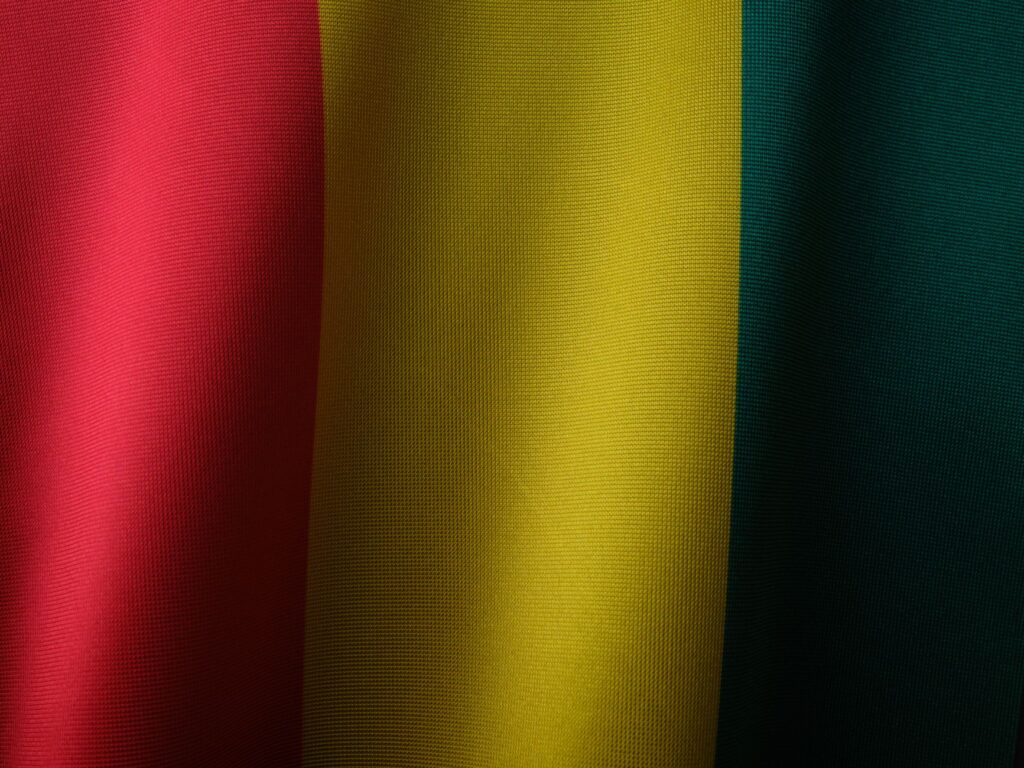 Close-up of the vibrant Guinea flag showing red, yellow, and green textile textures.