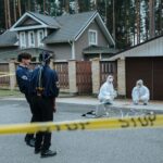 Police and forensic experts examining a crime scene in front of suburban houses.