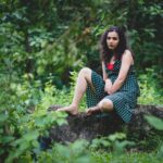 Woman in a green polka dot dress sitting on a rock in a lush forest setting.