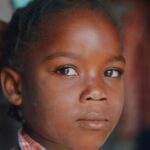 Close-up portrait of a young Haitian girl with expressive eyes and calm demeanor.