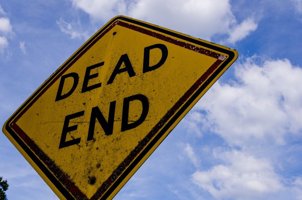 Yellow dead end sign against a blue sky with clouds, symbolizing stop or warning.