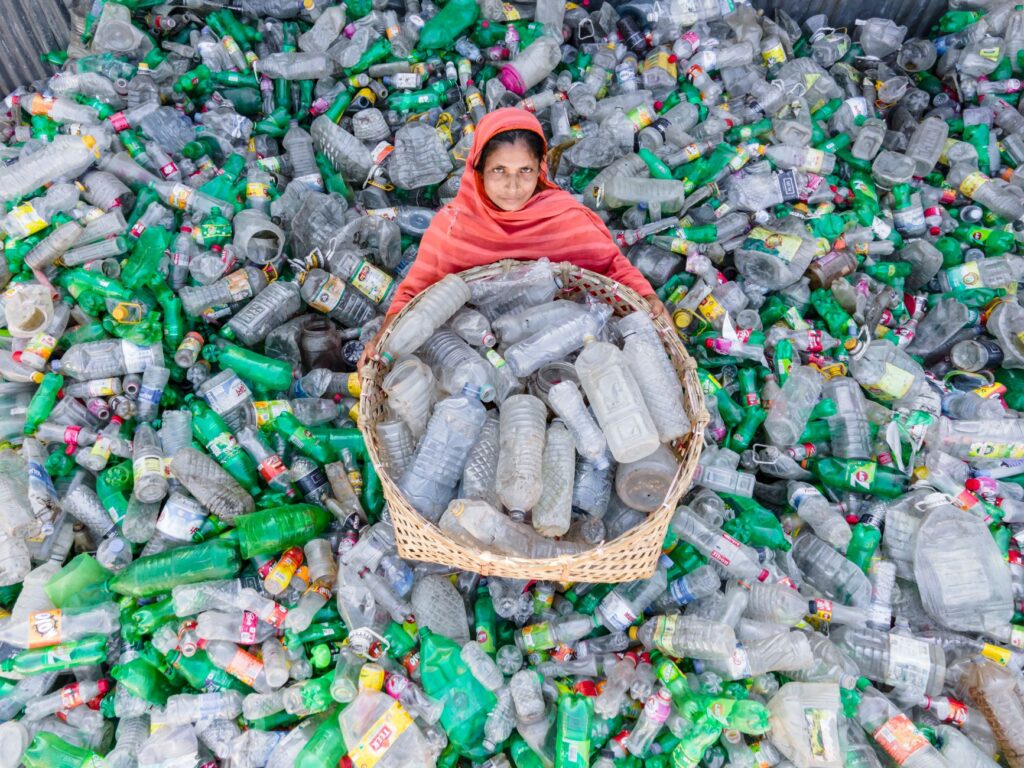 A woman in vibrant attire collects plastic bottles for recycling to promote environmental sustainability.