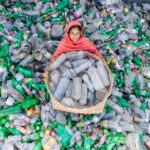 A woman in vibrant attire collects plastic bottles for recycling to promote environmental sustainability.
