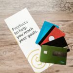 Assorted credit cards on a wooden table next to a leaflet with motivational text about financial goals.