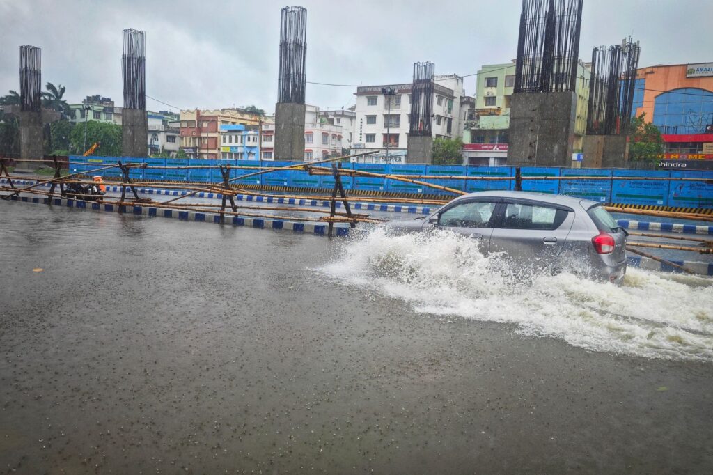 A car navigates a flooded street in Kolkata, India after heavy rain, showcasing urban challenges.