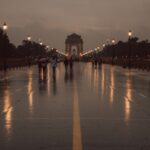 Moody evening scene at India Gate with reflections on the wet road and people walking.