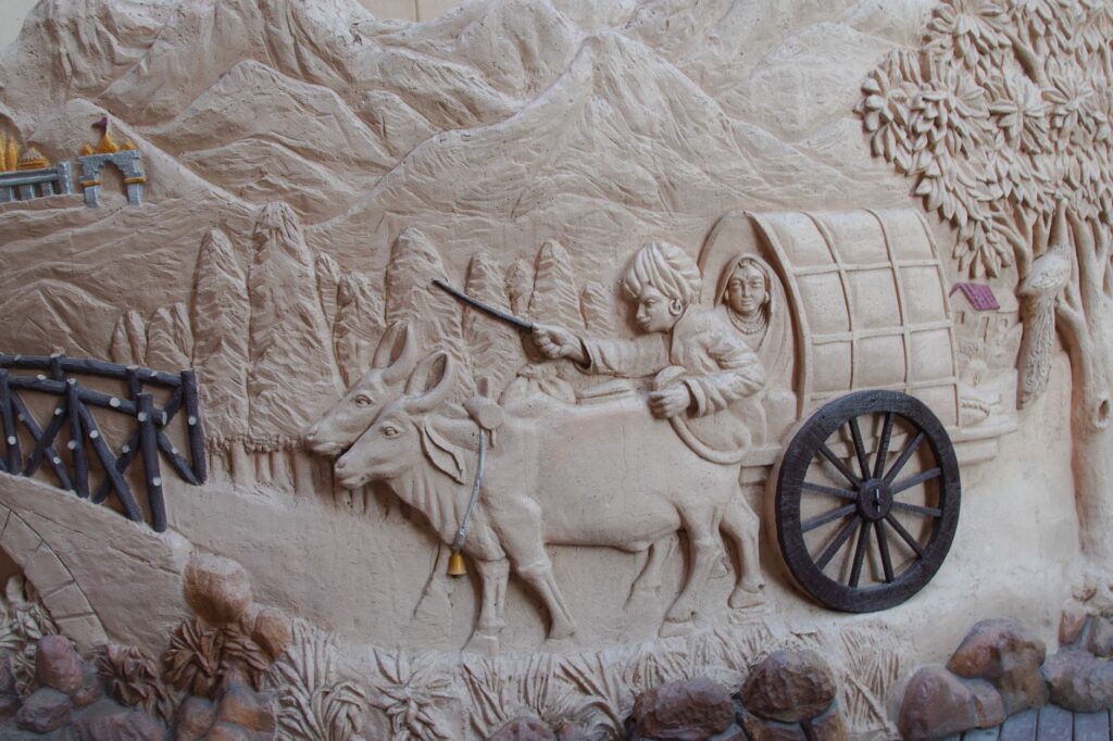 A detailed bas-relief depicting oxen pulling a wagon through a mountainous landscape, showcasing historical travel.