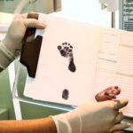 Healthcare professional handling newborn's footprint documentation in a hospital room.