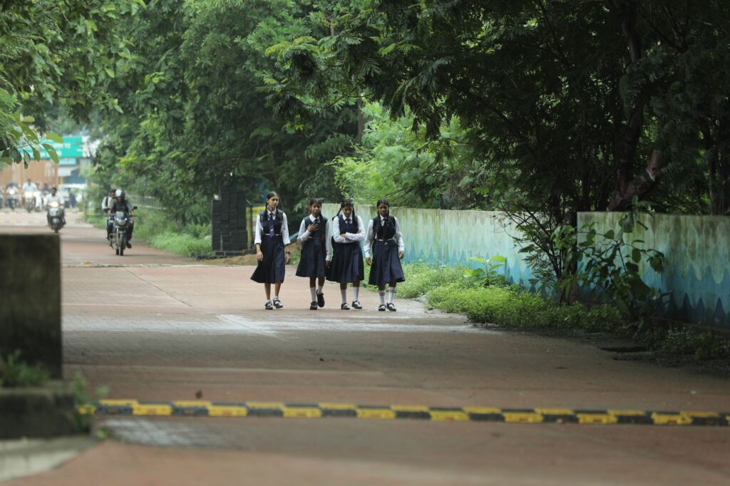 Four schoolgirls in uniform walking on a tree-lined path in Raipur, India.