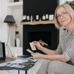 Woman with tarot cards using laptop for astrology reading in cozy living room.