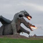 Majestic dragon sculpture breathing fire, set in an open park area, perfect attraction for fantasy lovers.