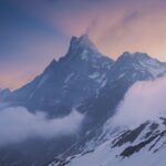 Stunning view of a snow-capped Himalayan mountain peak surrounded by clouds at sunset.