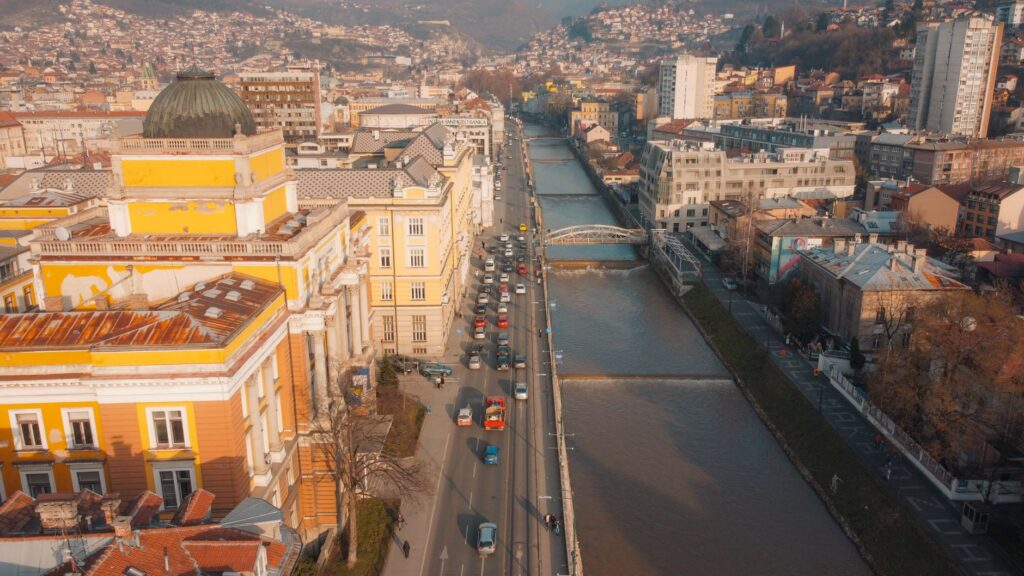 Aerial view of Sarajevo with Miljacka River, showcasing urban architecture and mountain backdrop.