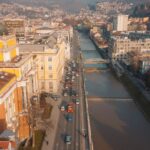 Aerial view of Sarajevo with Miljacka River, showcasing urban architecture and mountain backdrop.