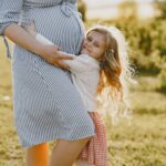 A pregnant mother enjoying a tender moment with her daughter in a sunny outdoor setting.