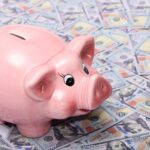Pink ceramic piggy bank placed on a spread of US dollar bills symbolizing savings and financial security.