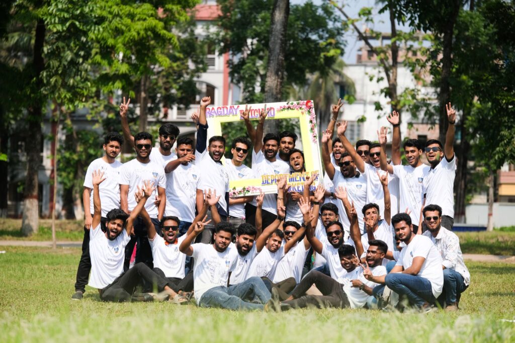 A joyful group of young men celebrating outdoors in a park during summer with a sign and white t-shirts.
