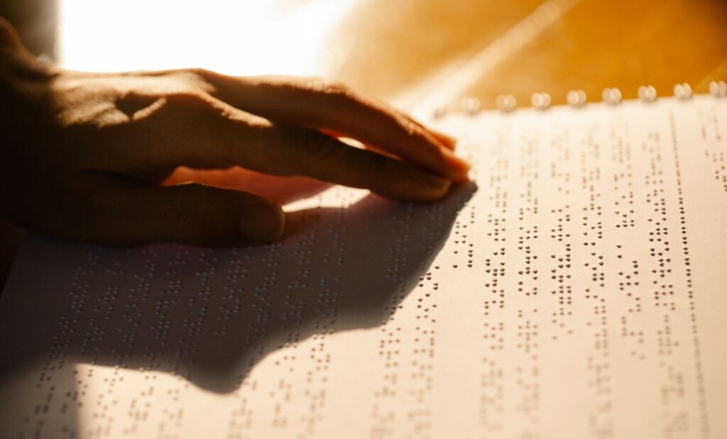 A close-up shot of a hand reading a Braille book, symbolizing tactile literacy for the visually impaired.
