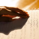 A close-up shot of a hand reading a Braille book, symbolizing tactile literacy for the visually impaired.