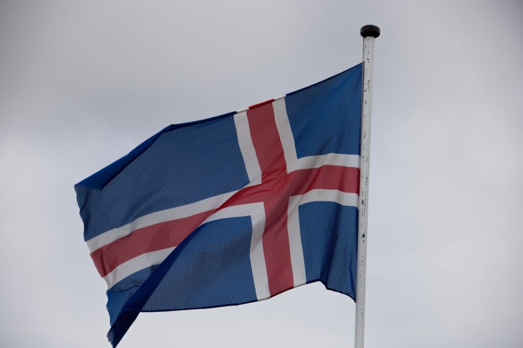 The national flag of Iceland waving atop a flagpole against a cloudy sky.