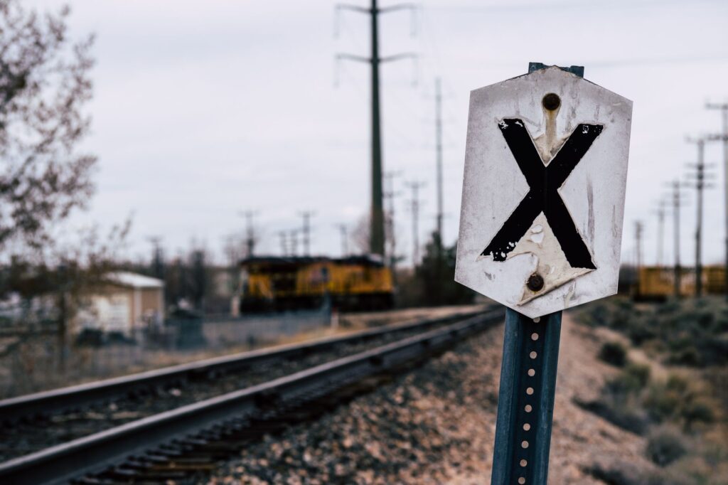 A weathered railroad crossing sign near train tracks with a freight train in the distance.