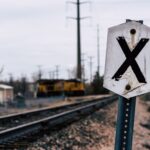 A weathered railroad crossing sign near train tracks with a freight train in the distance.