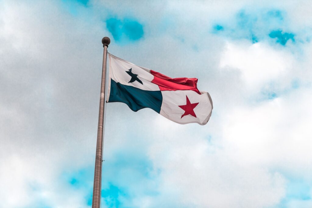 The flag of Panama waving on a flagpole with vibrant blue sky and clouds in the background.