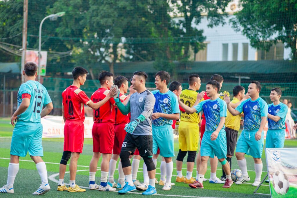Two soccer teams shake hands on the field in Hanoi, showcasing sportsmanship.