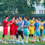 Two soccer teams shake hands on the field in Hanoi, showcasing sportsmanship.