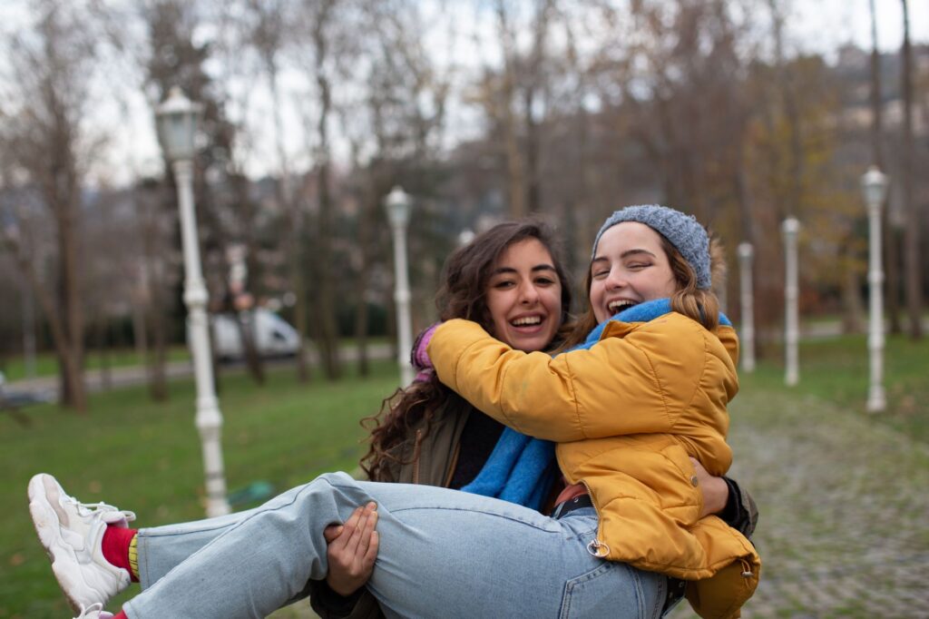 Two women laughing together outdoors in a park, symbolizing friendship and joy.