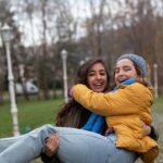 Two women laughing together outdoors in a park, symbolizing friendship and joy.