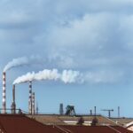 Factory chimneys emitting smoke over rooftops on a clear day, illustrating urban pollution.