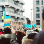 Peaceful protest in an urban setting featuring anti-war signage and Ukrainian flags.