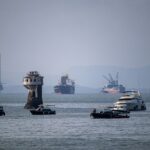 A scenic view of various ships and a tower in Mumbai harbor, India, with an oil rig in the background.