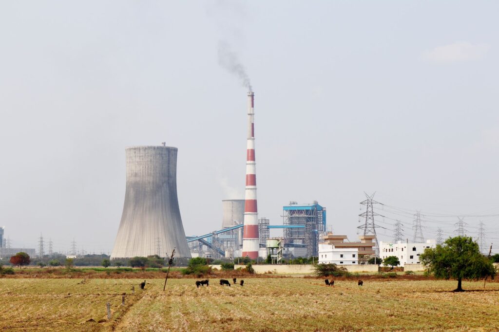 A cooling tower and smokestack in rural India, highlighting industrial and environmental contrasts.