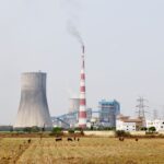 A cooling tower and smokestack in rural India, highlighting industrial and environmental contrasts.
