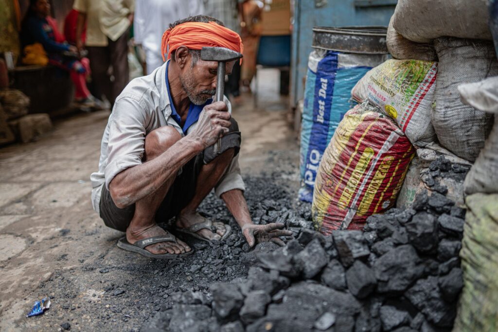 An adult man wearing an orange turban working with coal on a city street.
