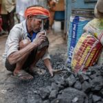 An adult man wearing an orange turban working with coal on a city street.