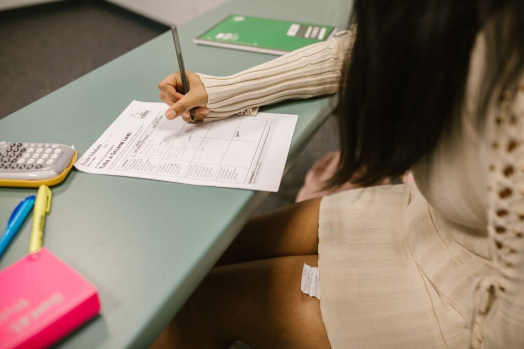 Student secretly looking at a cheat sheet under the desk while taking an exam in a classroom setting.