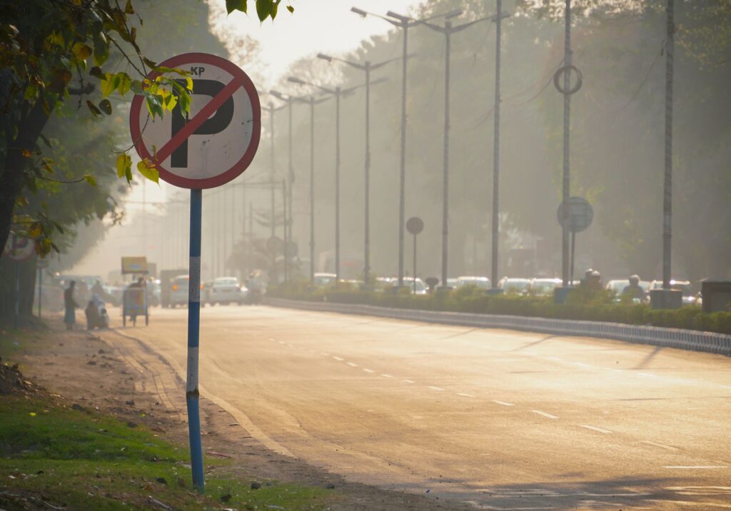 View of a bustling Indian street with a no parking sign, trees, and vehicles in the warm evening light.