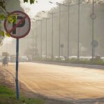 View of a bustling Indian street with a no parking sign, trees, and vehicles in the warm evening light.