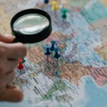 Magnifying glass focuses on pins highlighting travel destinations on a world map.