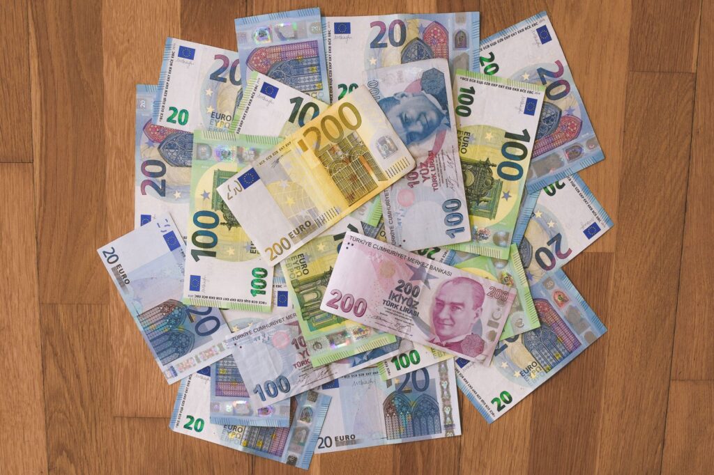 A pile of Euro and Turkish Lira banknotes scattered on a wooden surface, showcasing various denominations.