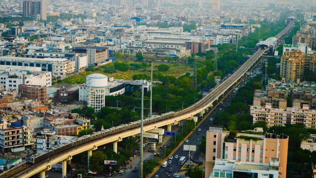 Aerial view of a metro train traversing an urban cityscape with dense buildings and greenery.