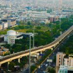 Aerial view of a metro train traversing an urban cityscape with dense buildings and greenery.